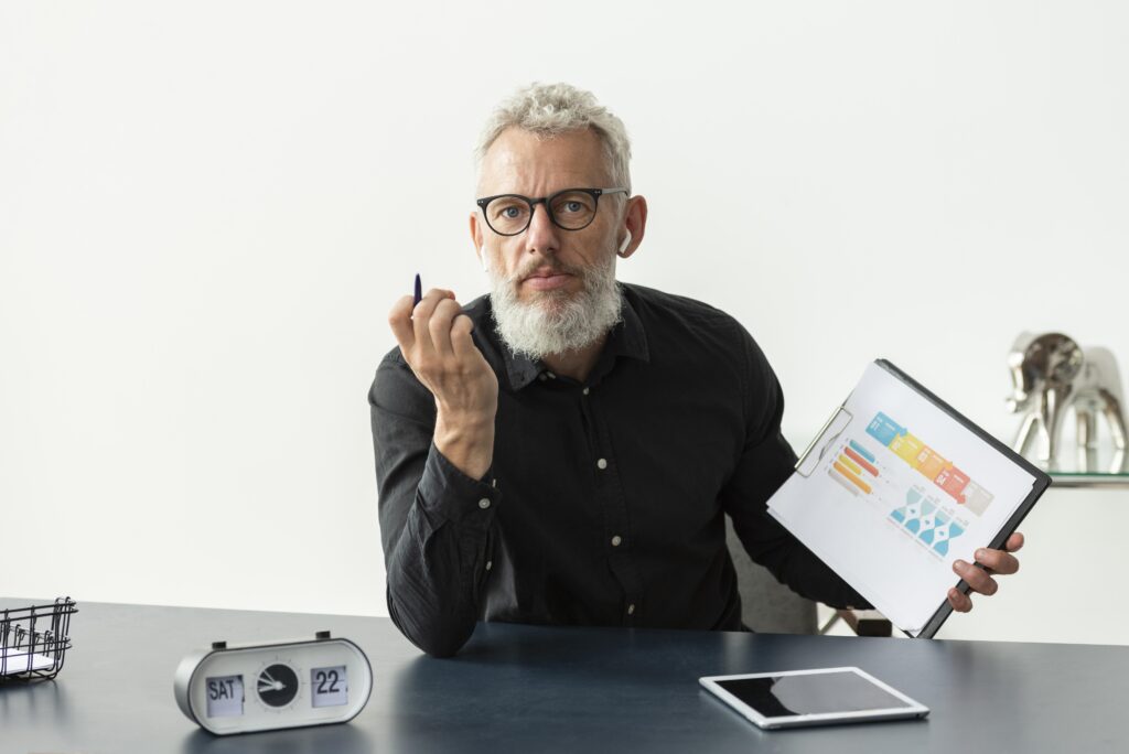 older-man-home-showing-graph-notepad-with-tablet-desk