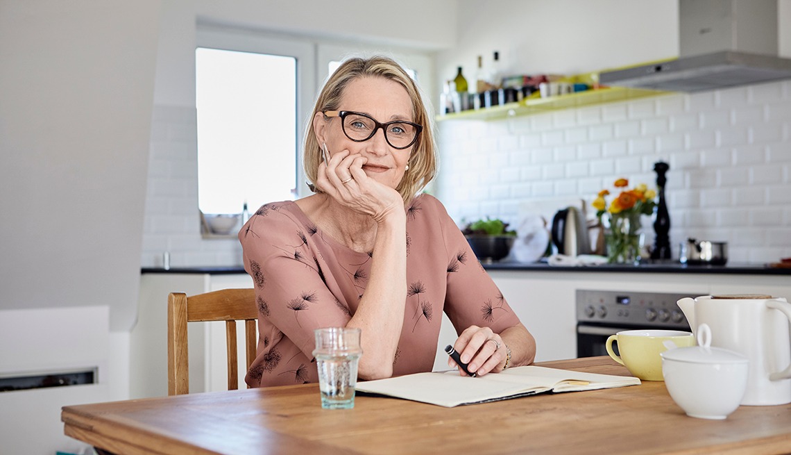 Woman sitting at her kitchen table writing in a journal Starting an Online Business For Seniors